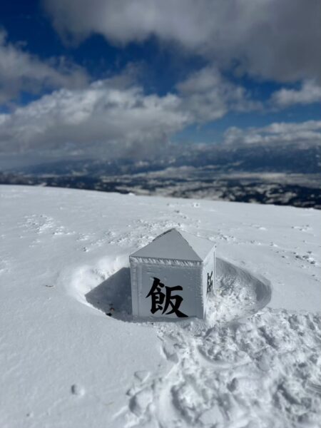 雪に覆われた飯縄山山頂の標柱で記念撮影