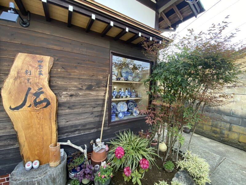 花と写真が飾られた割烹伝の店先の看板、佐渡の海鮮ランチの店