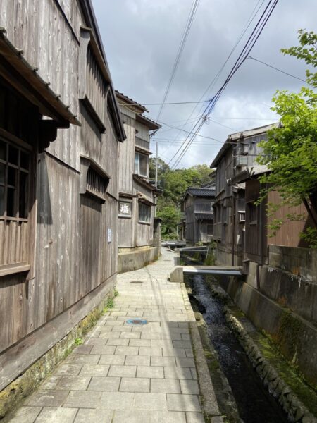 脇に水路が流れる宿根木の石畳の小道、生活感のある集落の風景