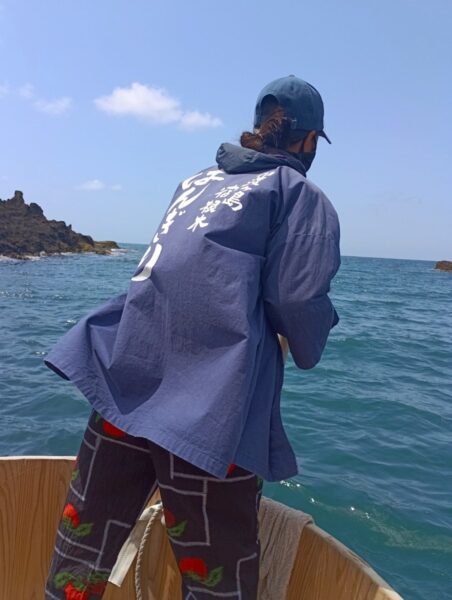 半纏姿の船頭が岩場の海でたらい舟を操る、佐渡小木の伝統漁の舟